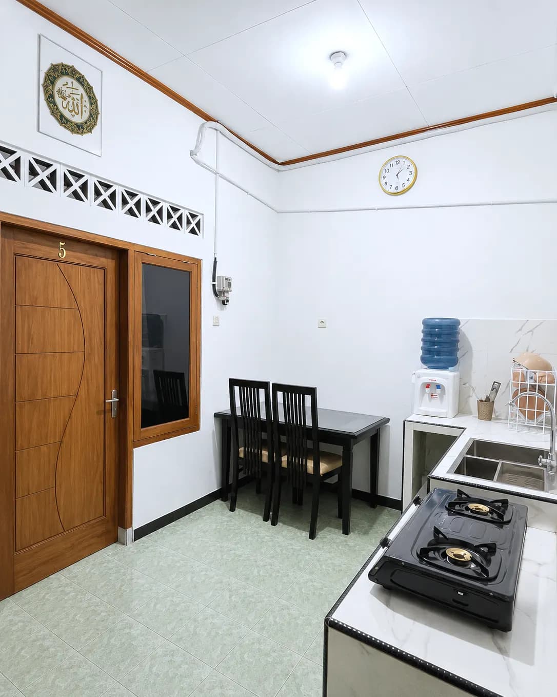Dapur lantai atas Kos Mbak Elis dengan kompor gas, wastafel, dispenser, dan meja makan