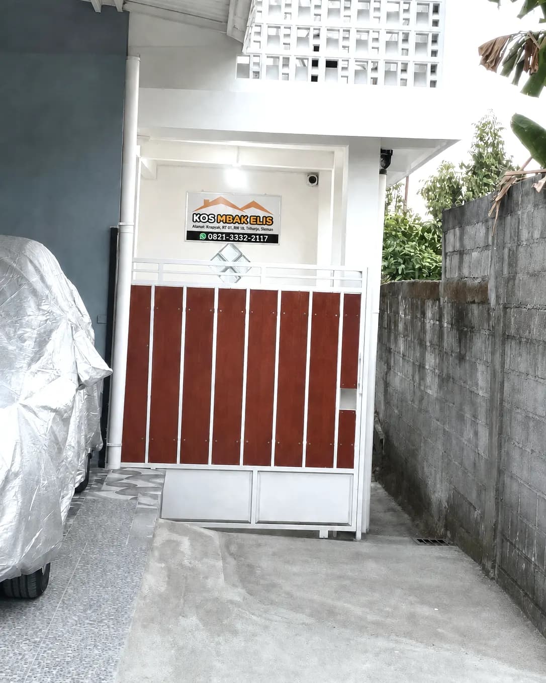 Gerbang depan Kos Mbak Elis dari jalan, dengan papan nama dan kamera CCTV di atas pintu masuk, Krapyak, Triharjo, Sleman